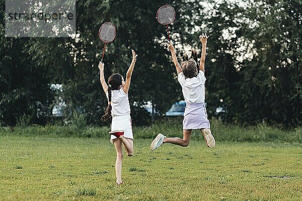 Rückansicht zwei Mädchen springen Park halten Badminton