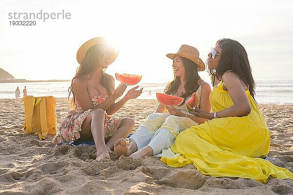 Freunde unterhalten sich beim Picknick am Strand bei Sonnenuntergang