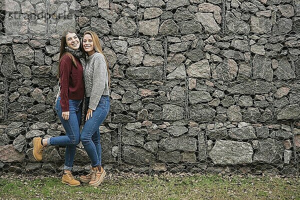 Zwei lächelnde junge Frauen vor einer Steinmauer
