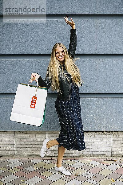 Fröhliche junge Frau mit Einkaufstüten an der Wand lehnend