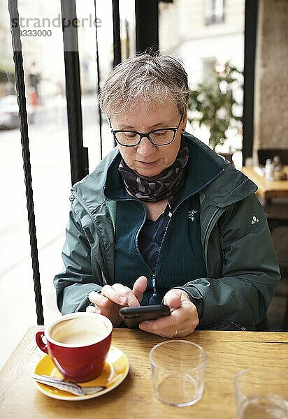 Ältere Frau  Best Ager  sitzt in Café  trinkt Kaffee  tippt Smartphone  Handy  Paris  Frankreich  Europa