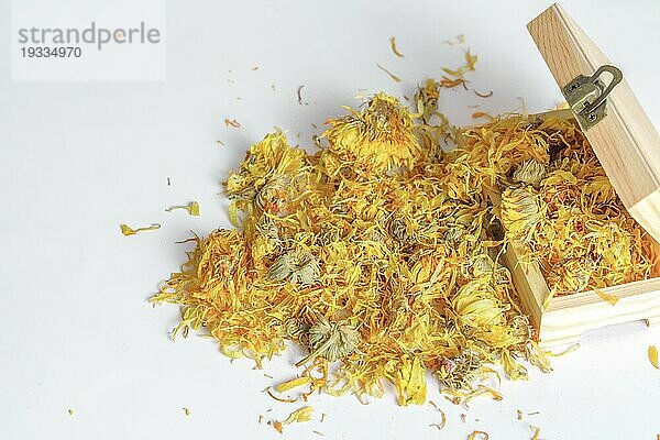 Calendula Blüten (Calendula officinalis)  getrocknete Blüten  die aus einer offenen Holzkiste kommen  vor weißem Hintergrund und Kopierraum