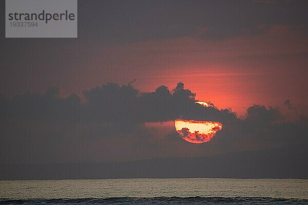Sonnenaufgang am Sandstrand. Landschaftsaufnahme mit roter kreisförmiger Sonne am Strand von Sanur  Bali  Indonesien  Asien