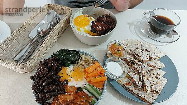 Draufsicht auf einen Mann  der sich zum Essen bereit macht  Jeyuk Deopbap  Bulgogi Bibimbap oder koreanische Reisschüssel und Quesadilla