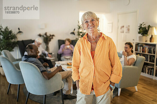 Porträt einer lächelnden älteren Frau im Ruhestand  die mit den Händen in den Taschen im Pflegeheim steht