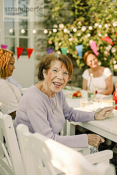 Porträt einer glücklichen älteren Frau  die am Esstisch im Hinterhof sitzt