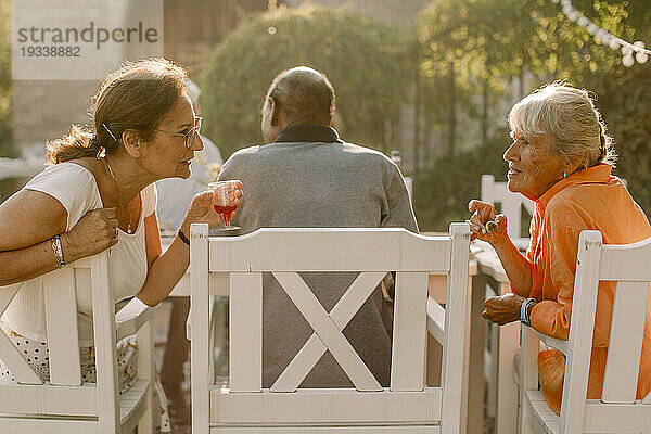 Ältere Frauen im Ruhestand reden hinter einem Mann  während sie im Hinterhof sitzen