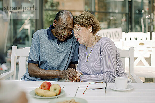 Älterer Mann und Frau halten Händchen  während sie am Esstisch sitzen