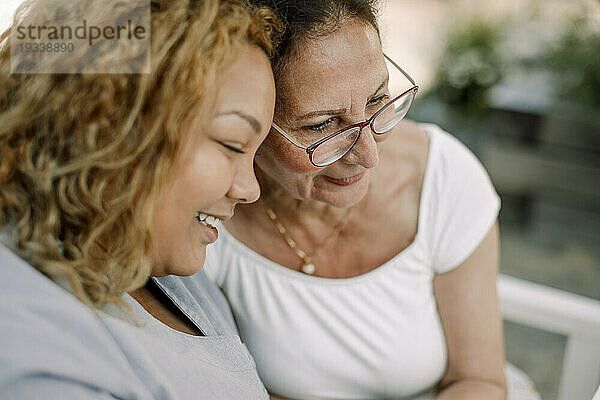 Lächelnde junge Pflegerin sitzt mit einer älteren Frau im Altersheim