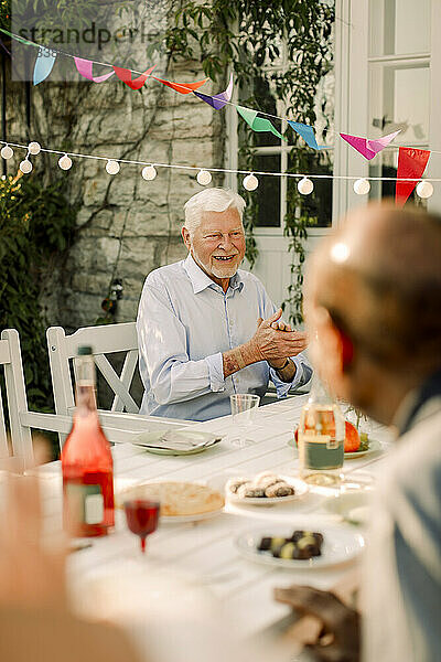 Glückliche ältere Männer sitzen am Esstisch im Hinterhof