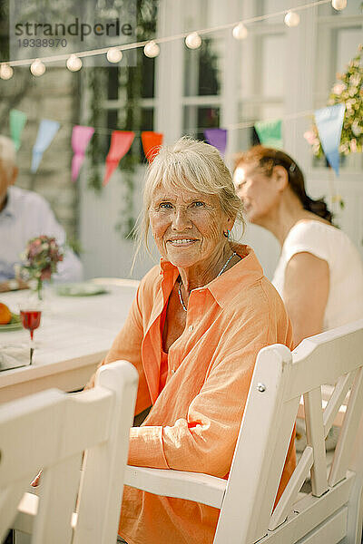 Porträt einer lächelnden älteren Frau  die auf einem Stuhl im Hinterhof sitzt