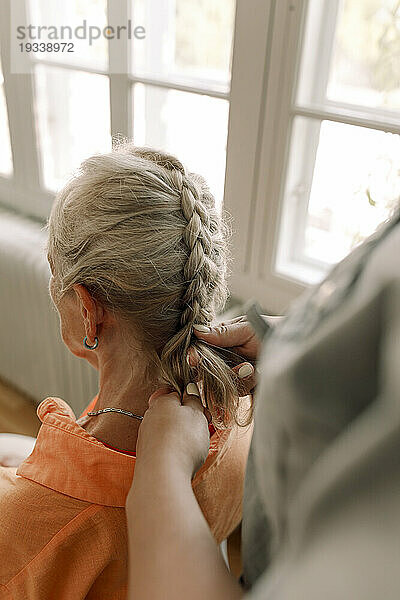 Mittelteil einer jungen Pflegerin  die einer Seniorin im Pflegeheim die Haare flechtet