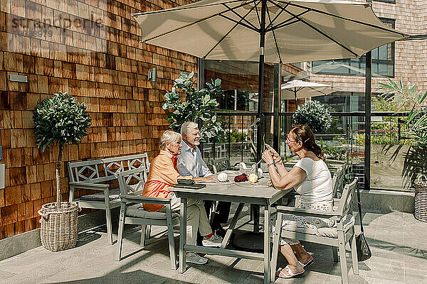 Ältere Männer und Frauen unterhalten sich  während sie an einem sonnigen Tag am Esstisch sitzen