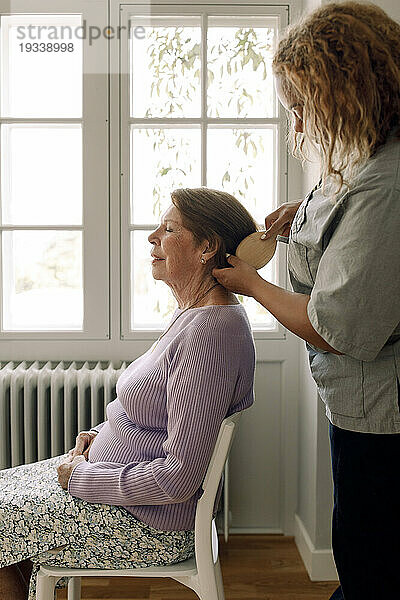 Seitenansicht einer jungen Krankenschwester  die einer älteren Frau im Altersheim die Haare bürstet