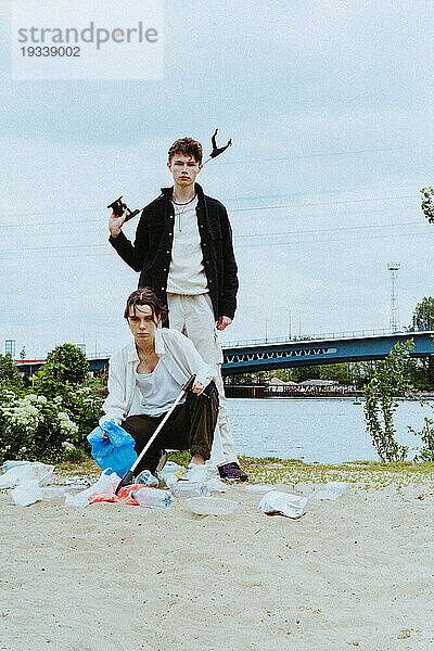 Ganzkörperporträt selbstbewusster junger Freunde  die Plastikmüll in der Nähe eines Flusses vor dem Himmel sammeln