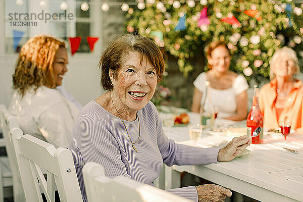 Porträt einer glücklichen Seniorin  die am Esstisch im Hinterhof sitzt