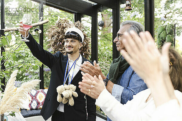 Junger Mann stößt Toast aus  während er mit der Familie steht und während der Party applaudiert