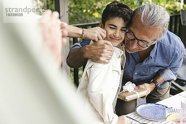 Älterer Mann umarmt Enkel während Mittsommer-Dinnerparty