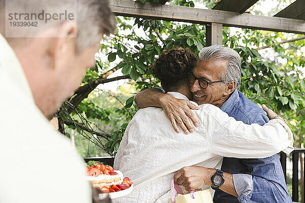 Glücklicher älterer Mann umarmt jungen Mann bei Dinnerparty