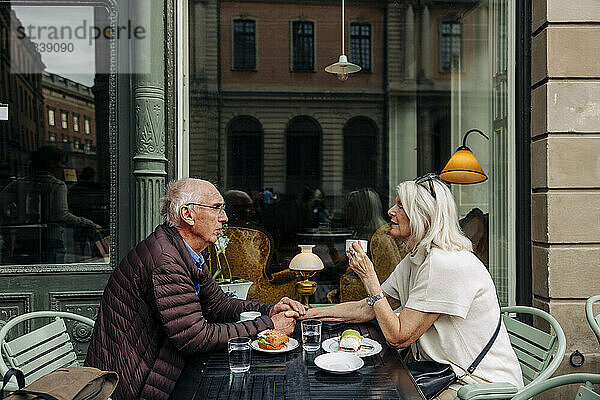 Älterer Mann hält die Hand einer Frau  während er zusammen im Straßencafé sitzt