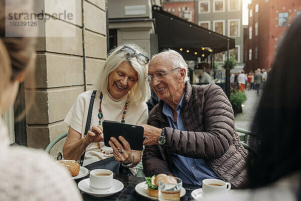 Glückliches älteres Paar teilt sein Smartphone  während es im Straßencafé sitzt