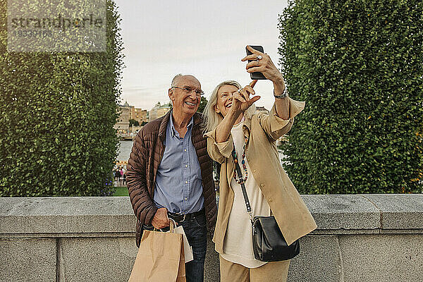 Glückliche Seniorin macht Selfie mit Mann  der sich am Geländer lehnt