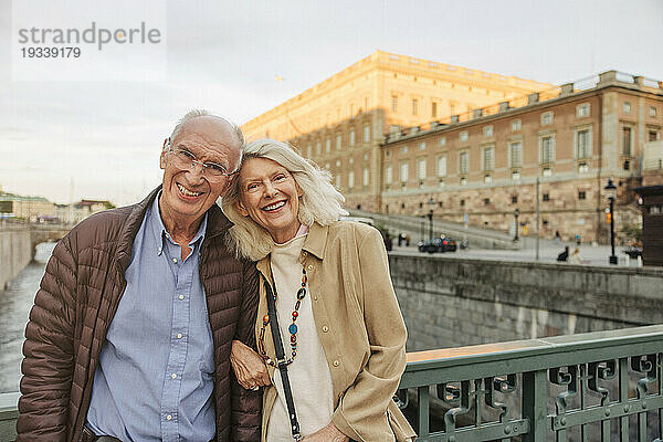 Porträt eines glücklichen älteren Mannes und einer glücklichen älteren Frau  die sich in der Stadt an ein Geländer lehnen