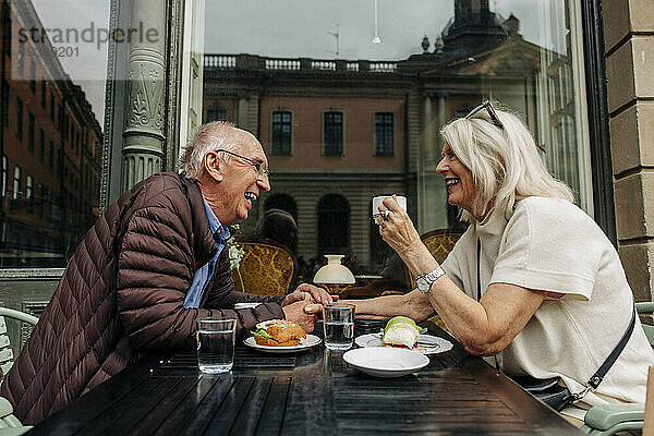 Glücklicher älterer Mann hält die Hand einer Frau  während er zusammen im Straßencafé sitzt