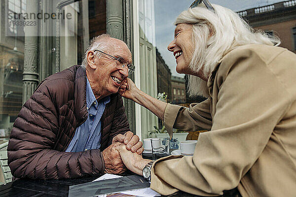 Liebevolle ältere Frau sitzt mit Mann Händchen haltend im Straßencafé