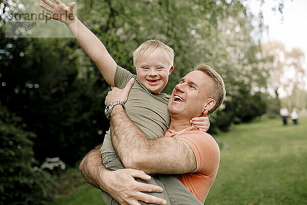 Glücklicher Mann trägt Sohn mit Down-Syndrom im Park