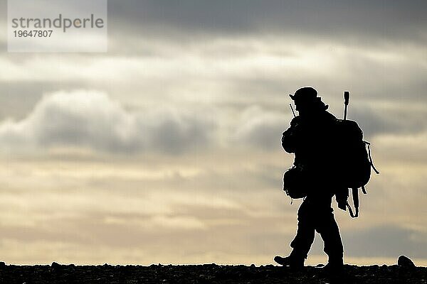 Silhouette eines gehenden Mannes mit Funkgerät  Gewehr und Rucksack  Spitzbergen  Svalbard  Norwegen  Europa