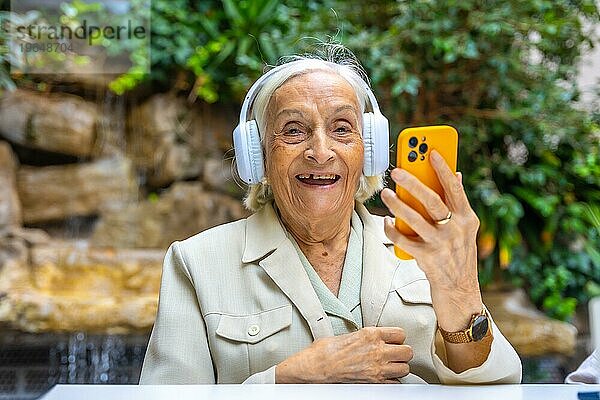 Glückliche ältere Frau mit Kopfhörer und Handy zum Musikhören in einer geriatrischen Einrichtung