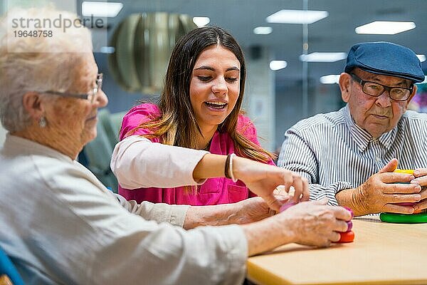 Freundliche Krankenschwester beaufsichtigt ältere Menschen beim Spielen von Geschicklichkeitsspielen im Pflegeheim