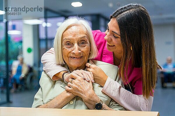 Krankenschwester umarmt von hinten eine nette ältere Frau in einer geriatrischen