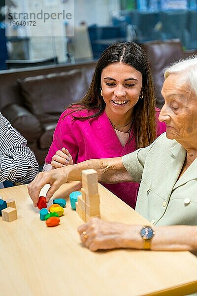 Vertikales Foto einer Krankenschwester  die älteren Menschen in einem Pflegeheim beim Spielen hilft