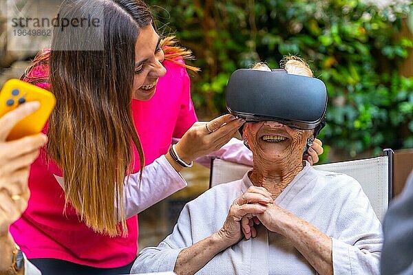 Krankenschwester  die eine ältere Frau mit einer Virtual Reality Brille in einer geriatrischen Einrichtung betreut