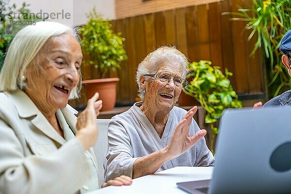 Glückliche Frauen winken während eines Videogesprächs in einer geriatrischen Einrichtung. Einführung von Technologie für Senioren