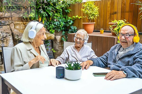 Glückliche ältere Menschen  die im Garten eines Pflegeheims mit Kopfhörern Musik genießen