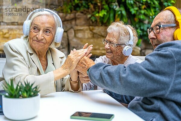 Senioren genießen Musik mit Kopfhörern in einem Garten eines Pflegeheims
