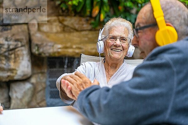 Glückliche ältere Menschen  die Kopfhörer benutzen und lächelnd in einem Garten in einer geriatrischen Einrichtung sitzen