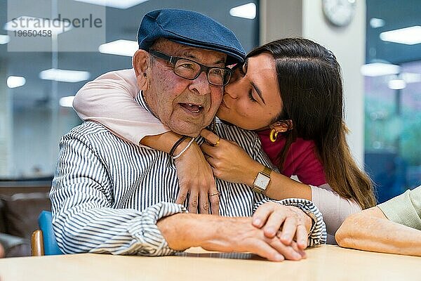 Zärtlicher Moment einer Krankenschwester  die einen älteren Mann in einer geriatrischen Einrichtung küsst und umarmt