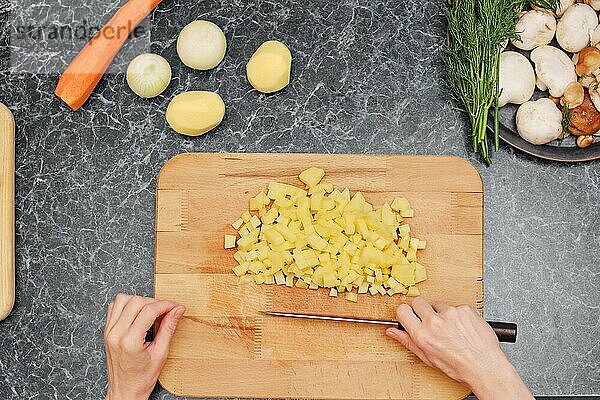 Draufsicht auf die Hände einer Frau beim Kartoffelschneiden in der Küche
