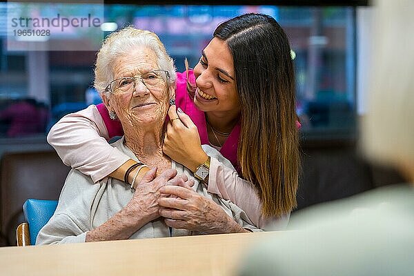 Zärtlicher Moment einer glücklichen Krankenschwester  die eine alte Frau in einer geriatrischen Einrichtung streichelt und umarmt