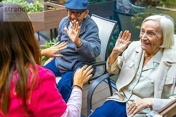 Ältere Menschen amüsieren sich mit einer Krankenschwester  die in einem Garten in einer geriatrischen Einrichtung sitzt