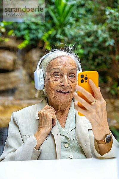 Vertikales Porträt einer älteren Frau  die mit dem Telefon Musik hört  in einer geriatrischen Einrichtung