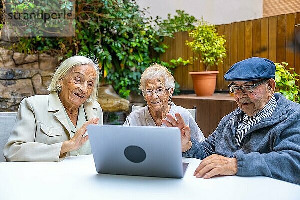 Ältere Menschen winken während eines Videoanrufs mit Laptop in einer geriatrischen Einrichtung