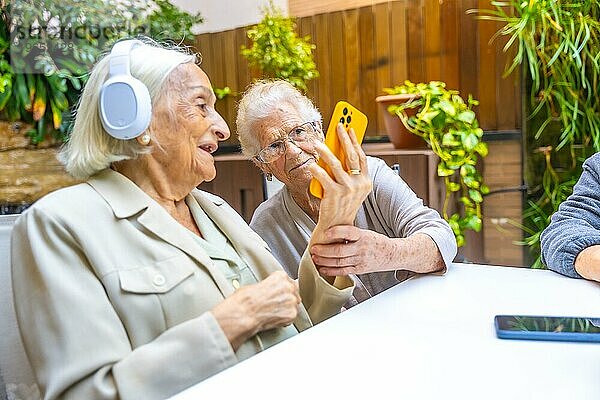 Senioren hören Musik mit Handy und Kopfhörer in einer geriatrischen Einrichtung