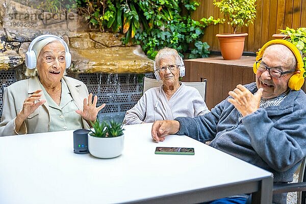 Drei fröhliche und niedliche Senioren  die in einer geriatrischen Einrichtung mit Kopfhörern Musik hören