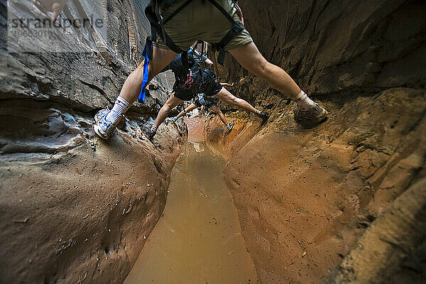 Drei Menschen zwängen sich zwischen zwei Wänden über Wasser im Slot Canyon  Utah.
