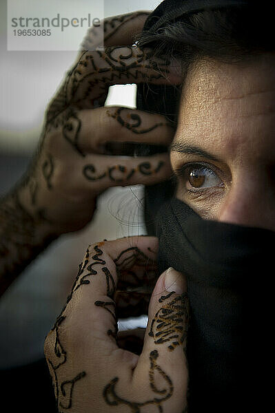 Eine Frau mit Henna-Tattoos zieht ihren schwarzen Schal über ihr Gesicht.